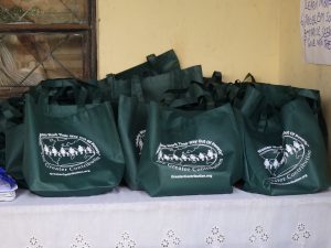 A table with many green bags full of supplies to be distributed, each bag has the Greater Contribution logo.